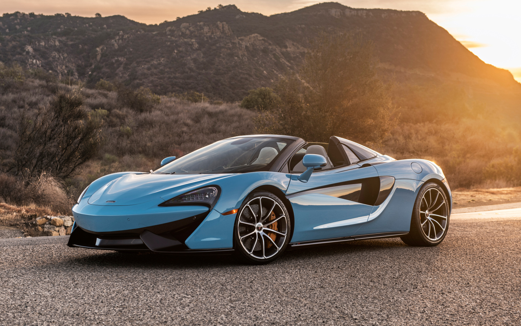 Голубой спортивный автомобиль  McLaren 570S Spider, 2018 на фоне солнца