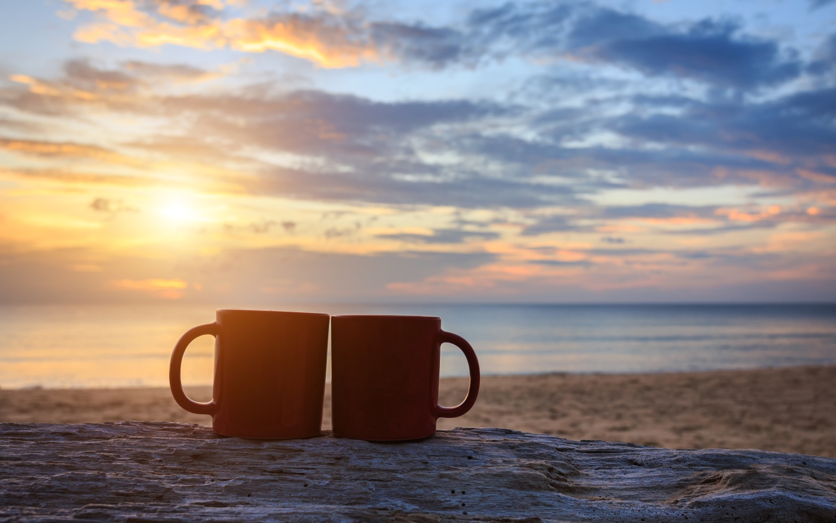Two cups are standing on the sand against the background of dawn