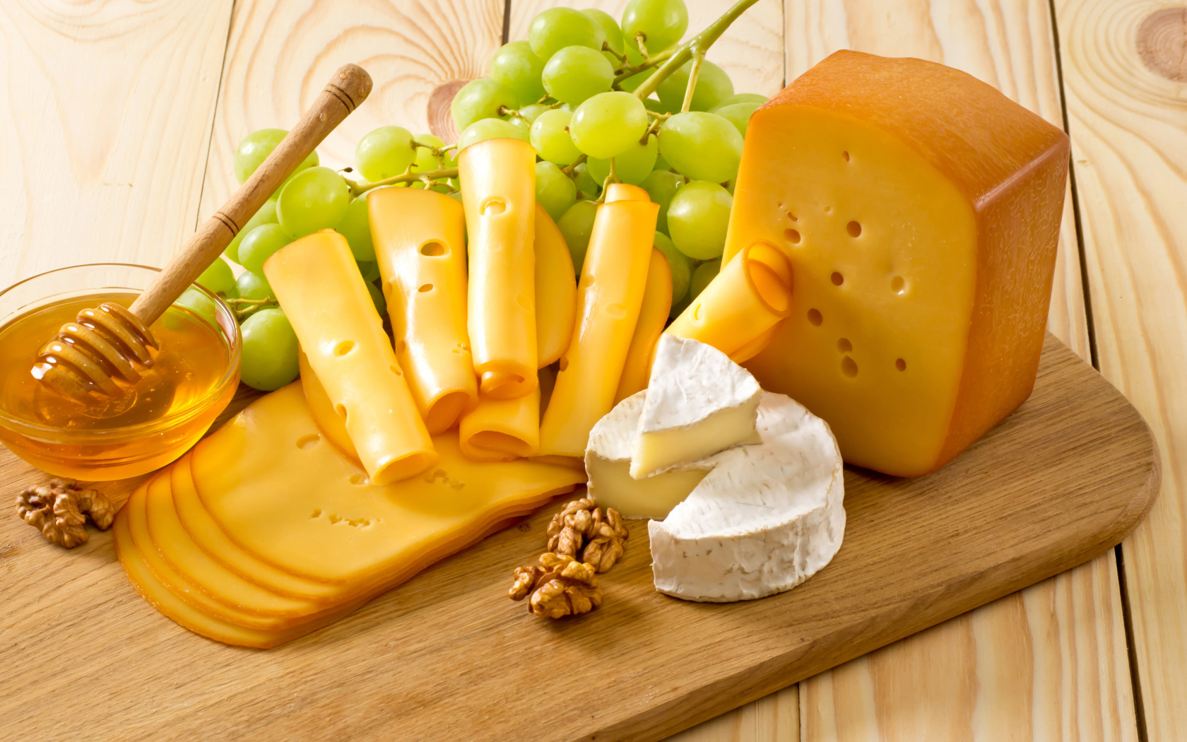 Cheese on the table with white grapes, honey and nuts