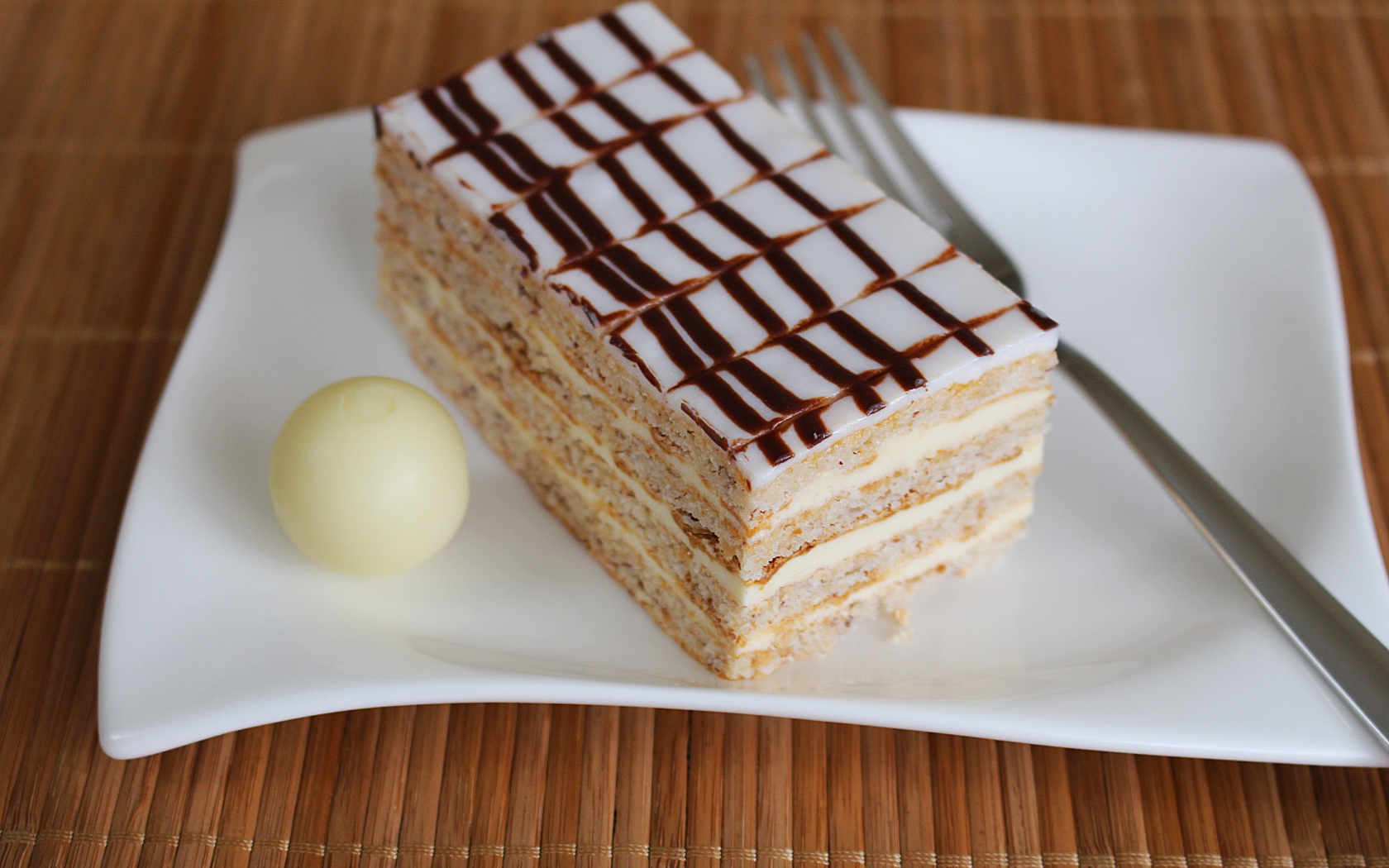 Кусок торта на белой тарелке с вилкой и конфетой 