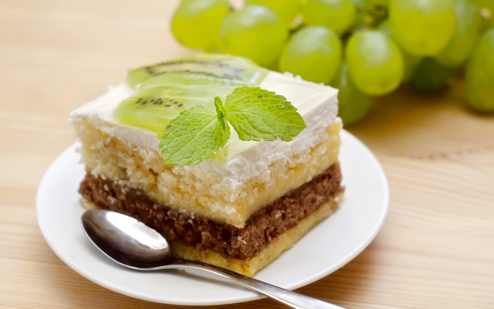 Кусок торта с киви и мятой на столе с виноградом