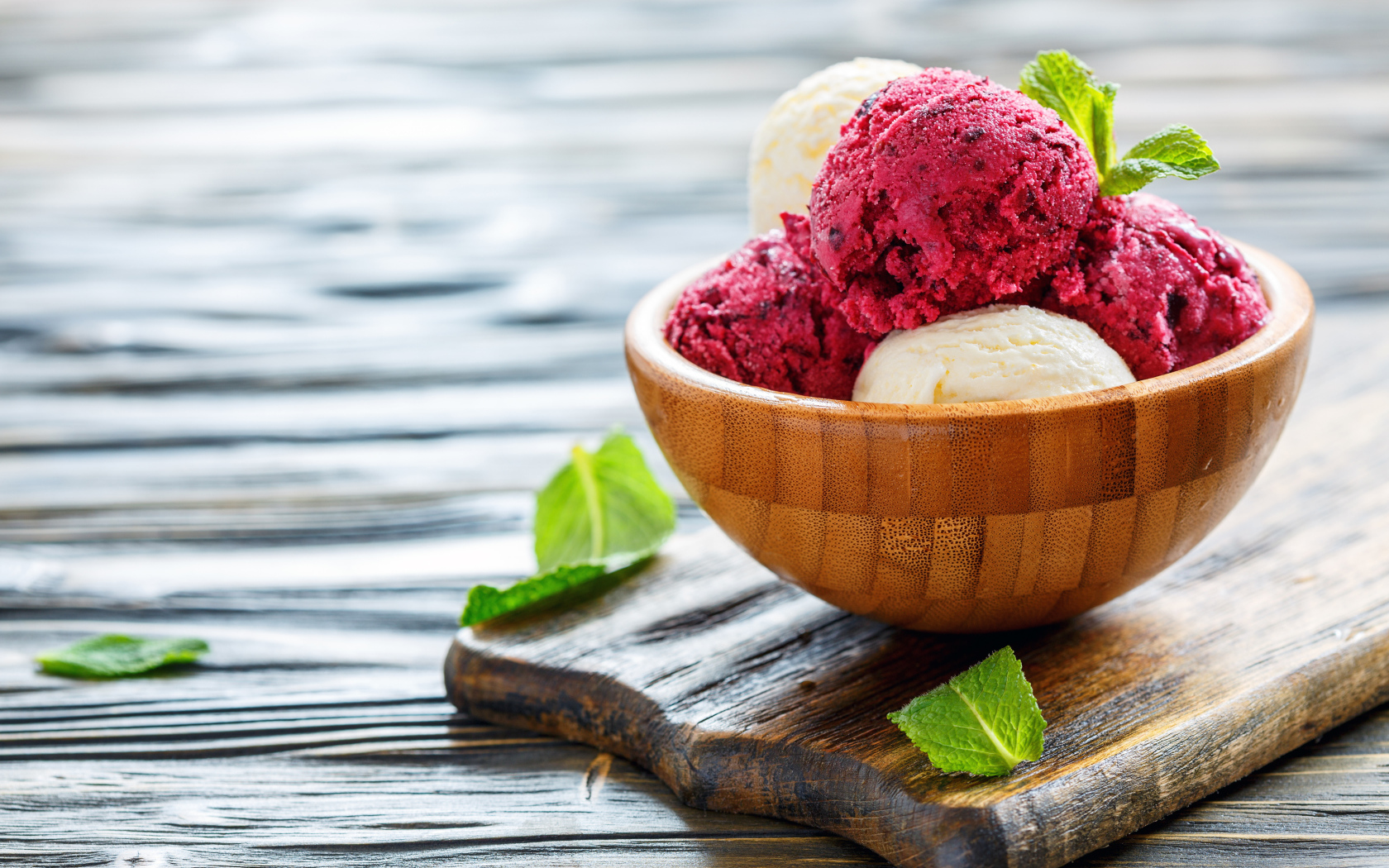 Шарики фруктового и ванильного мороженого в деревянной миске на столе