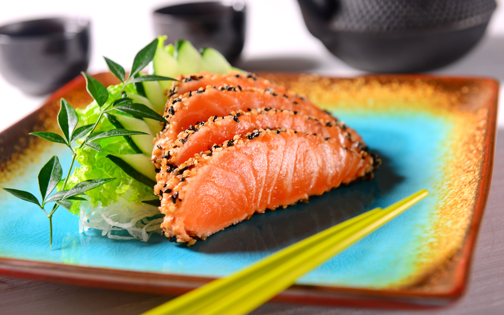 Красная рыба с листьями салата и свежими огурцами на тарелке с палочками