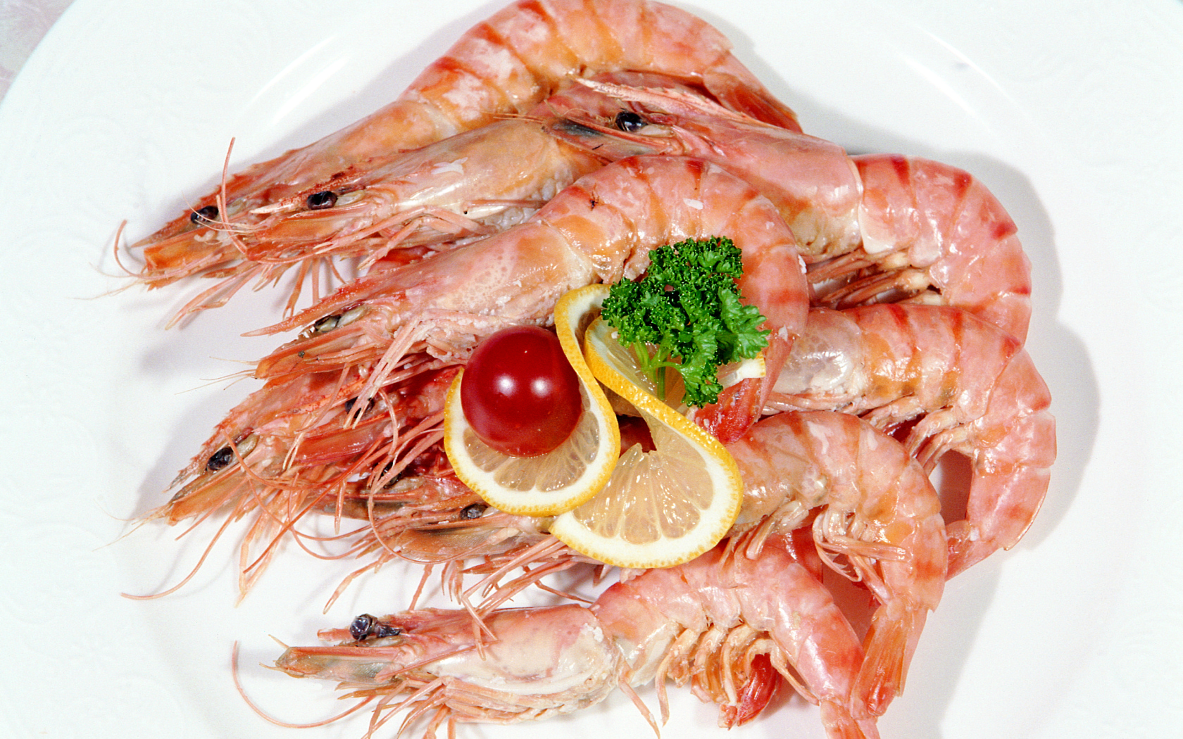 Креветки с лимоном и помидором на белой тарелке
