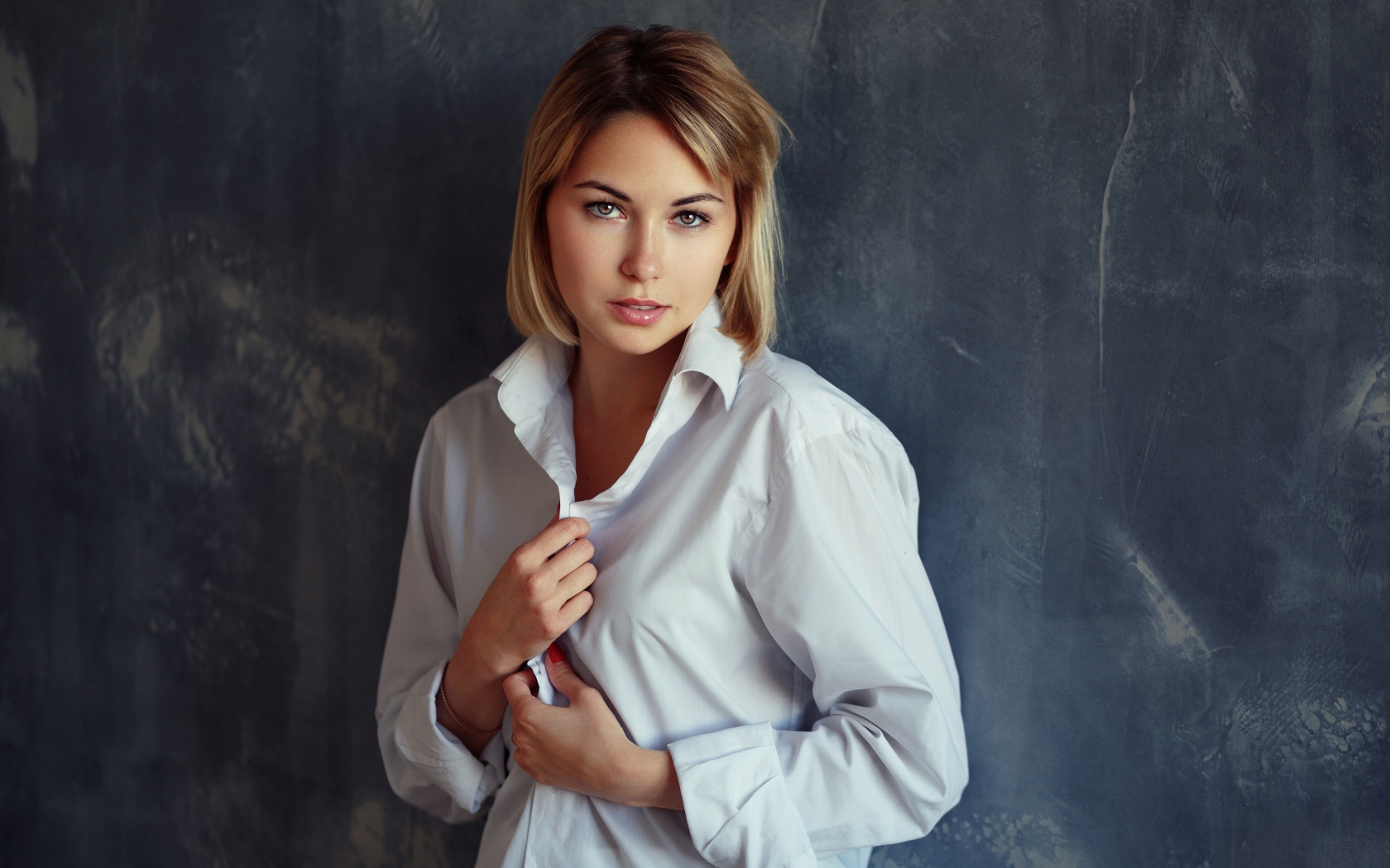 Красивая девушка блондинка в белой рубашке у стены 