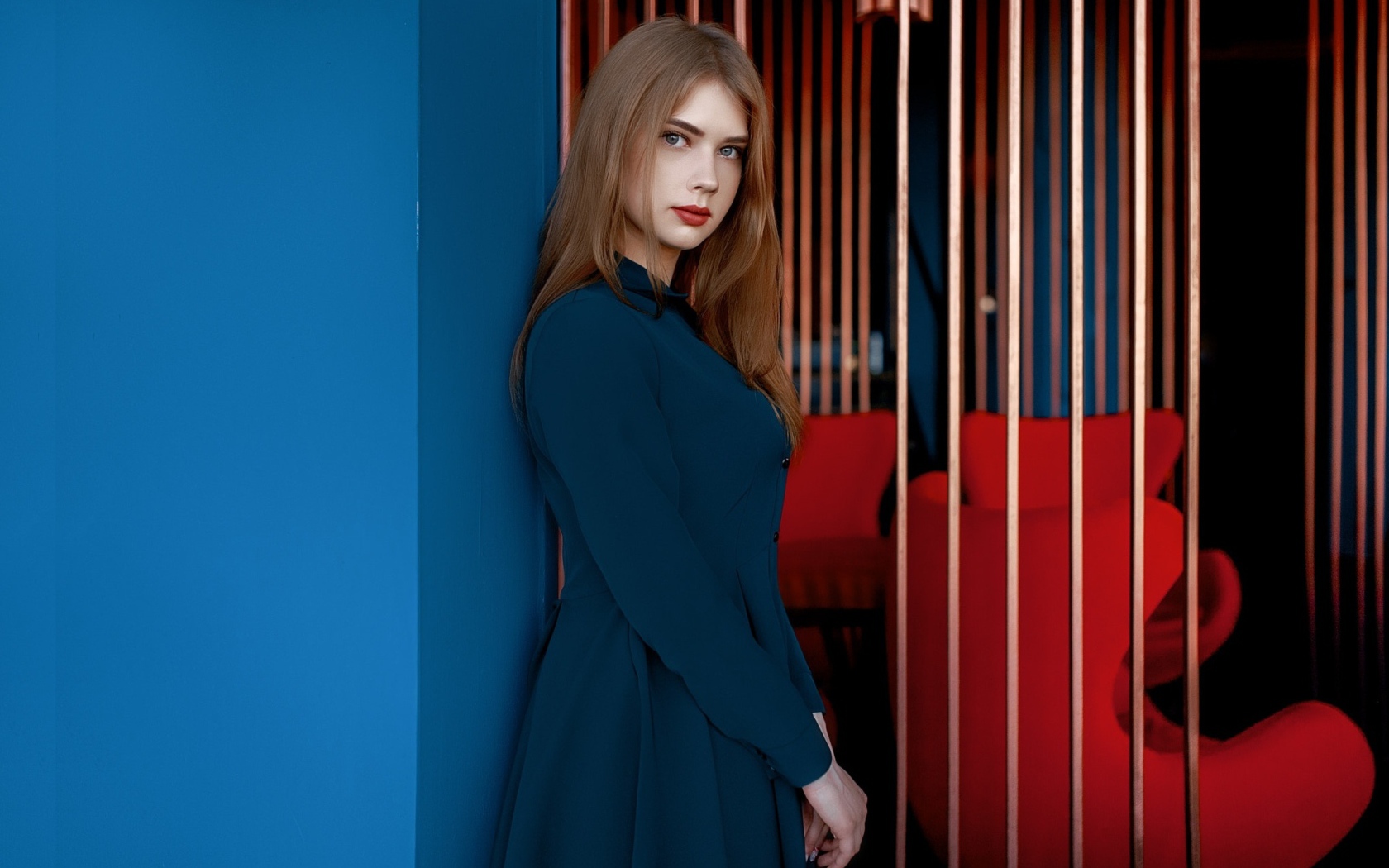 Красивая голубоглазая девушка стоит в пальто у стены