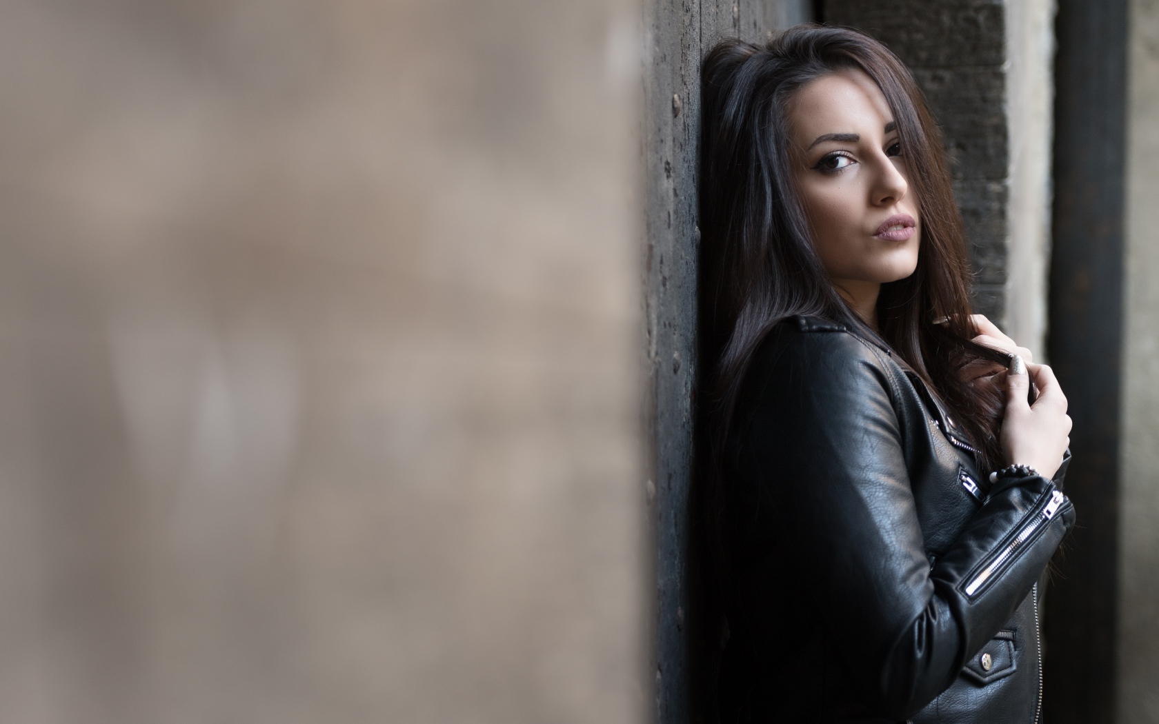 Красивая  брюнетка в кожаной куртке стоит у стены