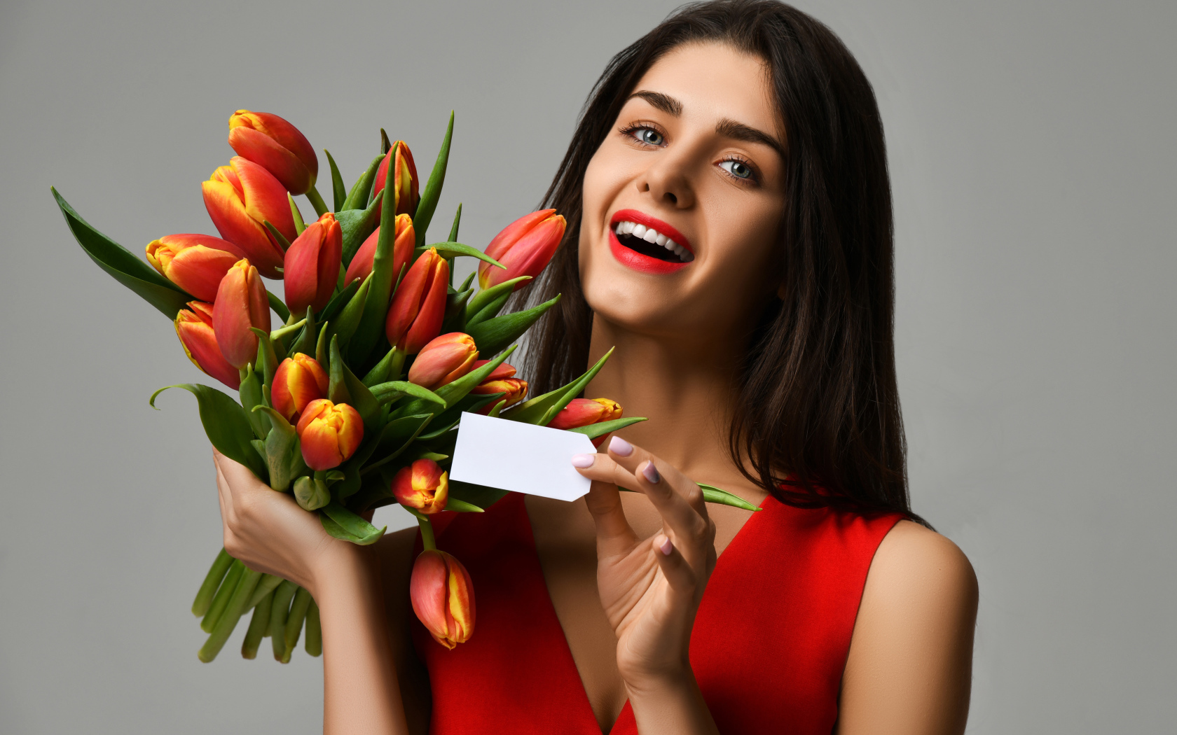 Красивая брюнетка с букетом тюльпанов на сером фоне
