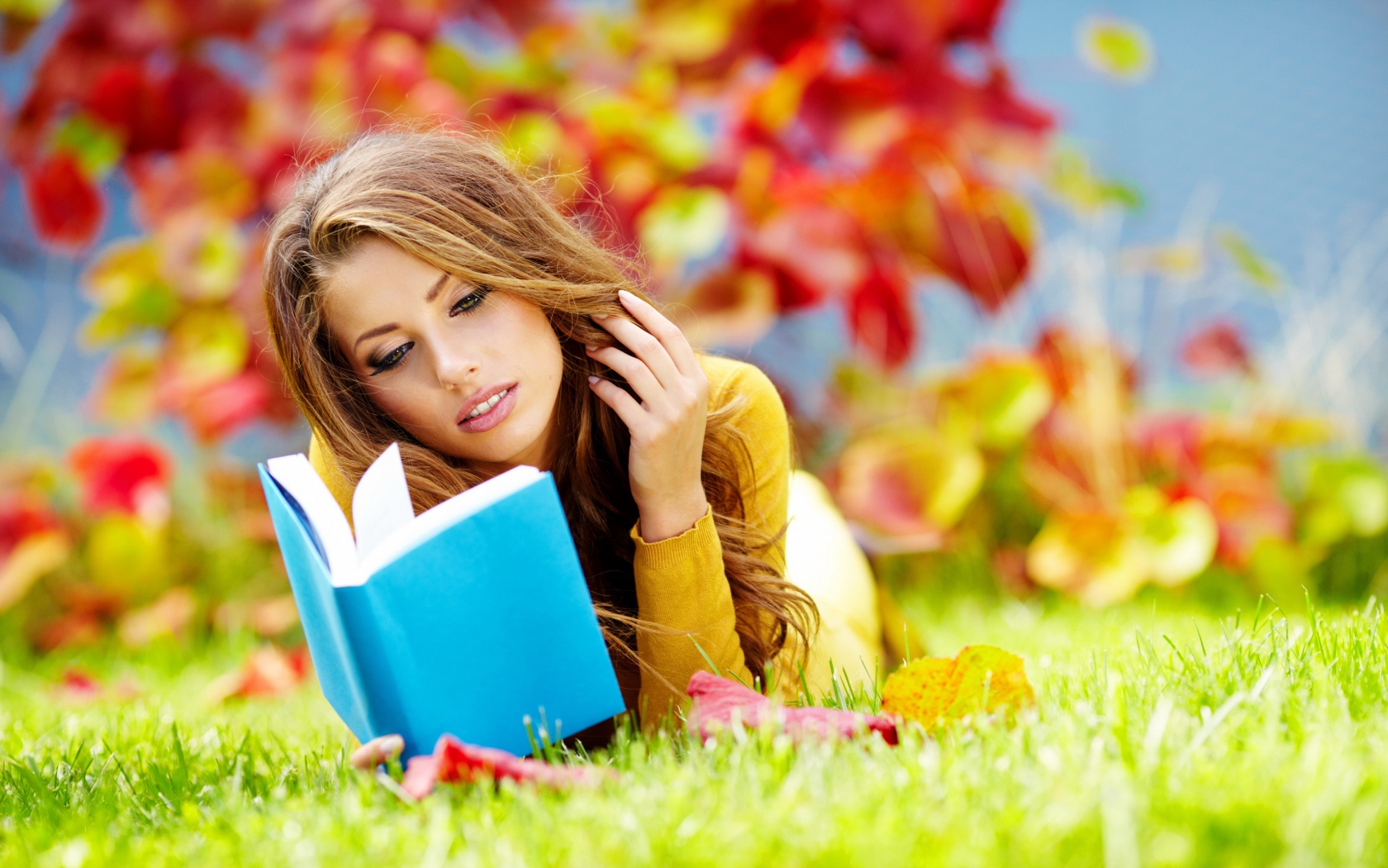 Красивая девушка читает книгу лежа на зеленой траве