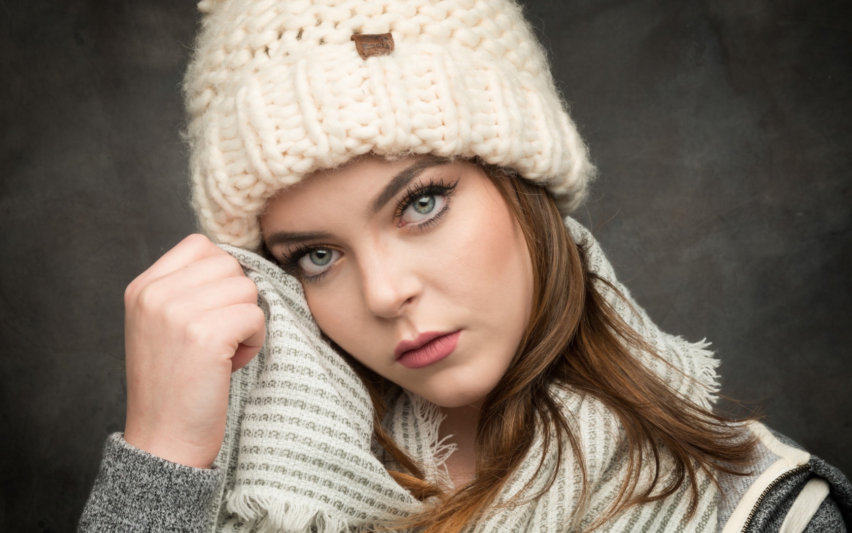 Красивая зеленоглазая девушка в белой вязаной шапке с шарфом