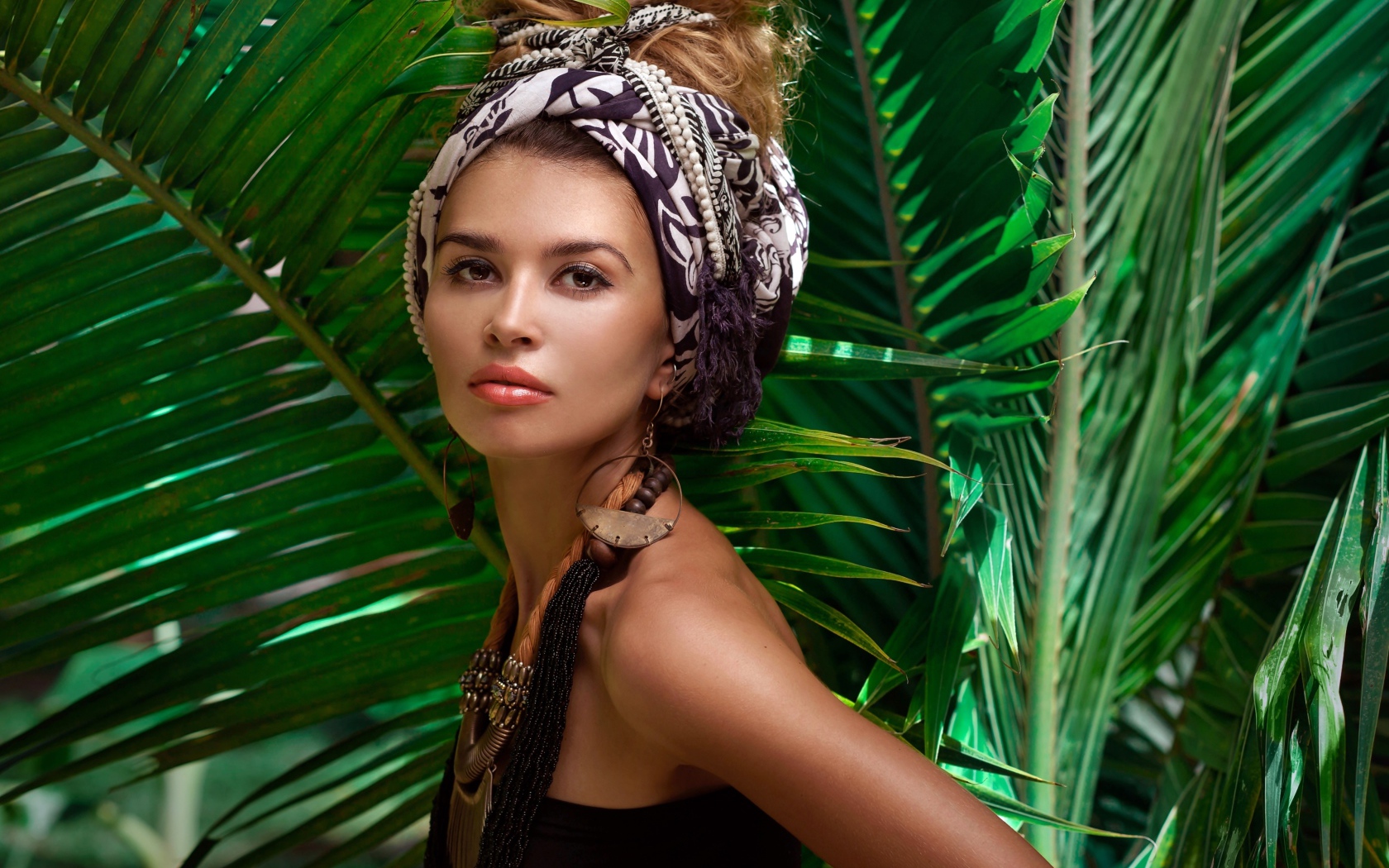 Красивая женщина в тюрбане с украшениями среди зеленых пальмовых листьев