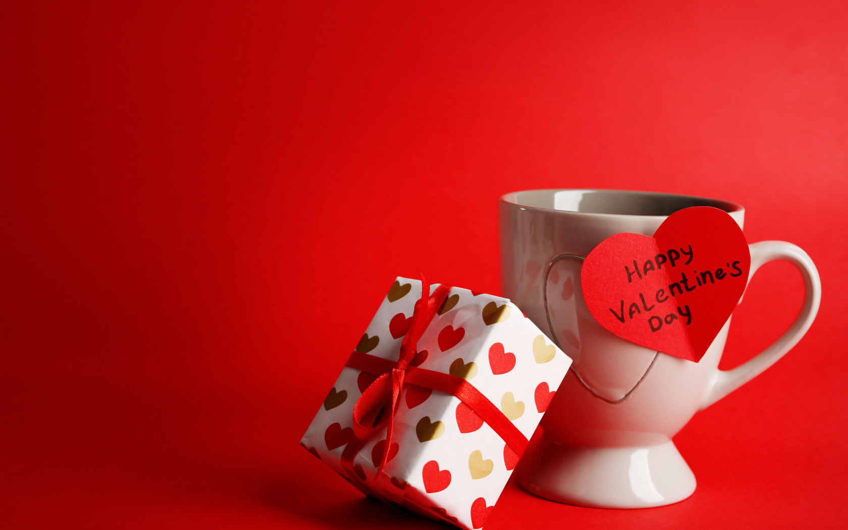 Чашка с подарком и валентинкой на красном фоне на 14 февраля