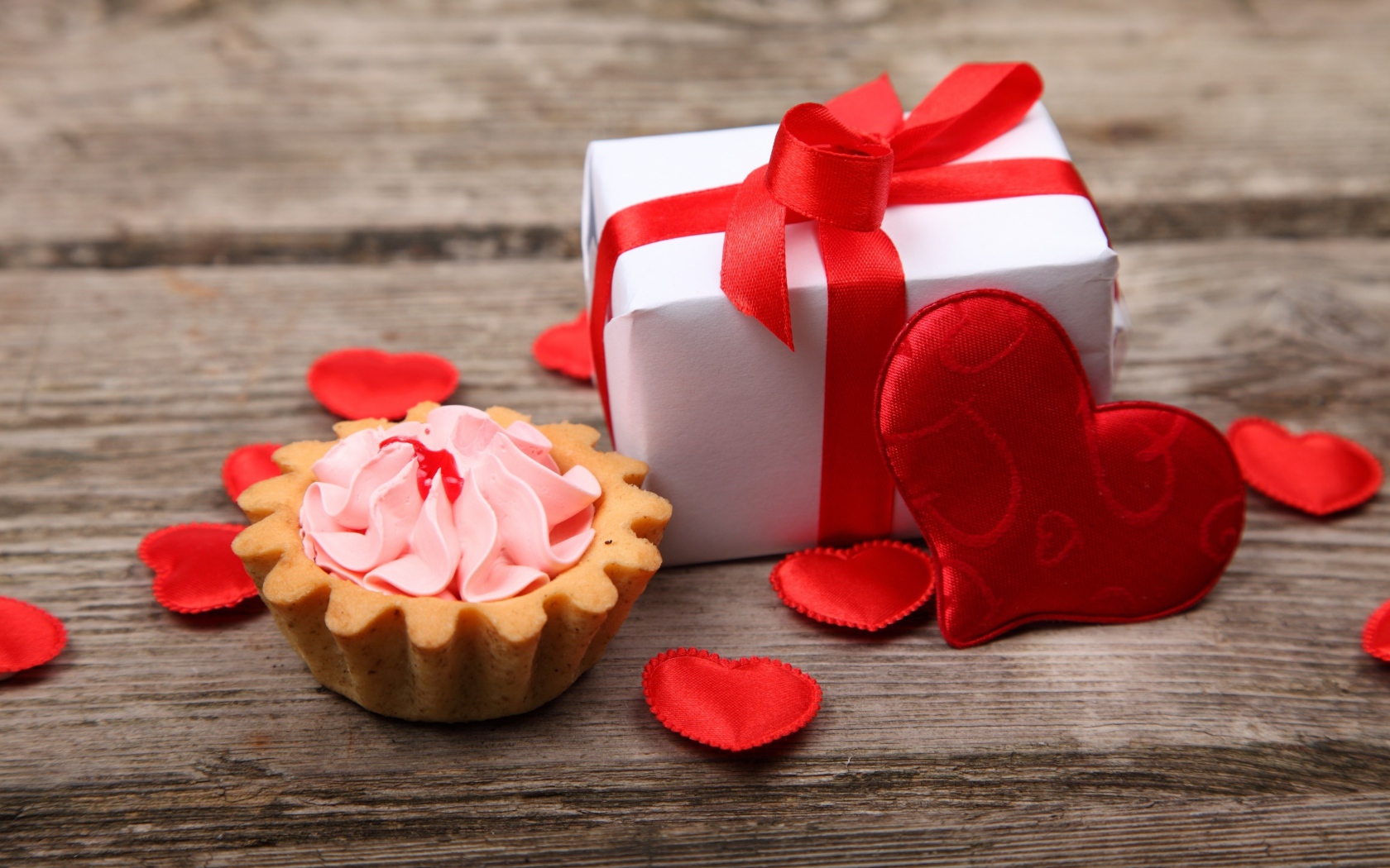 Пирожное, подарок и сердечки на деревянном фоне на День Святого Валентина