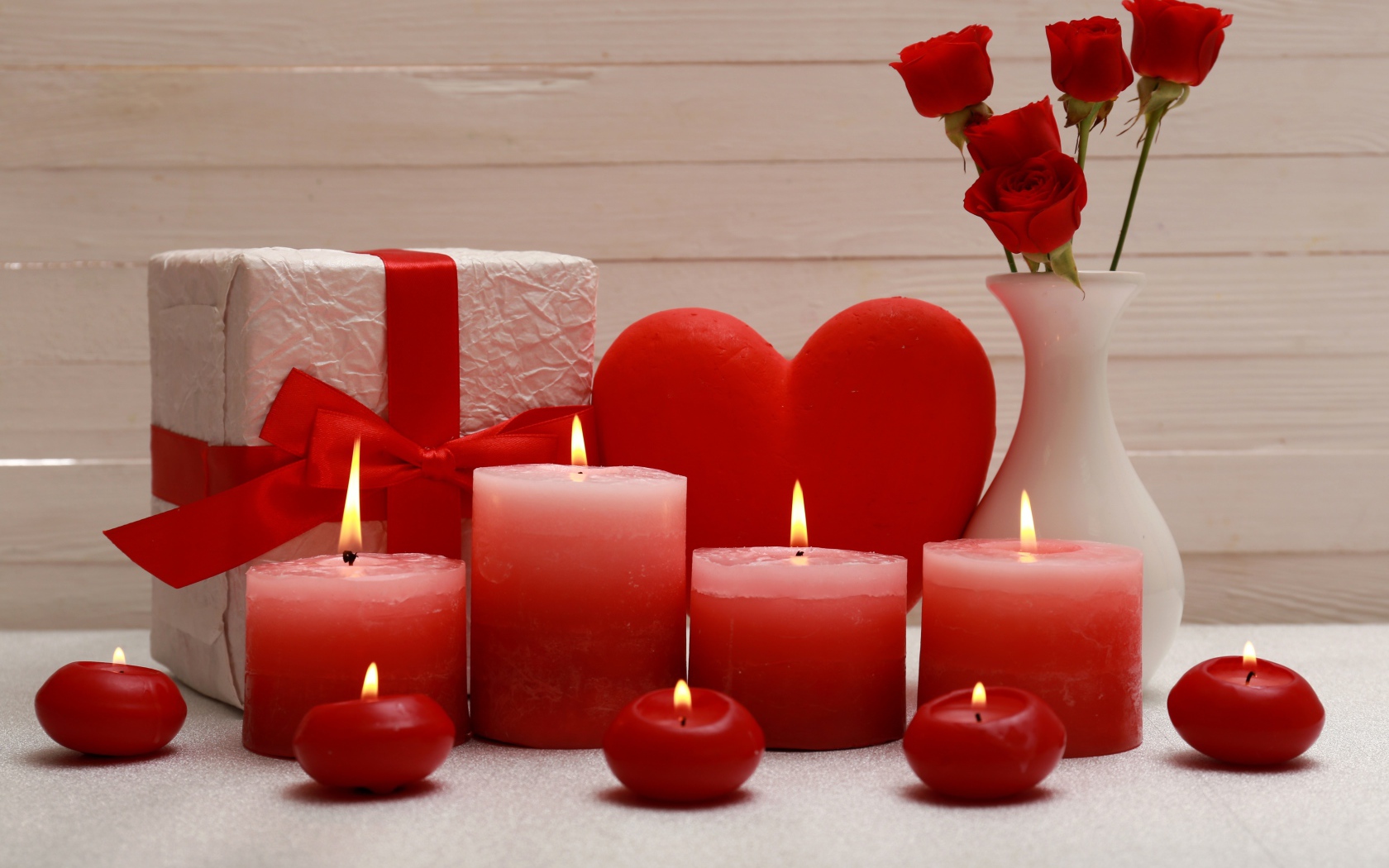 Lighted red candles on the table with a gift, red heart and flowers in a vase