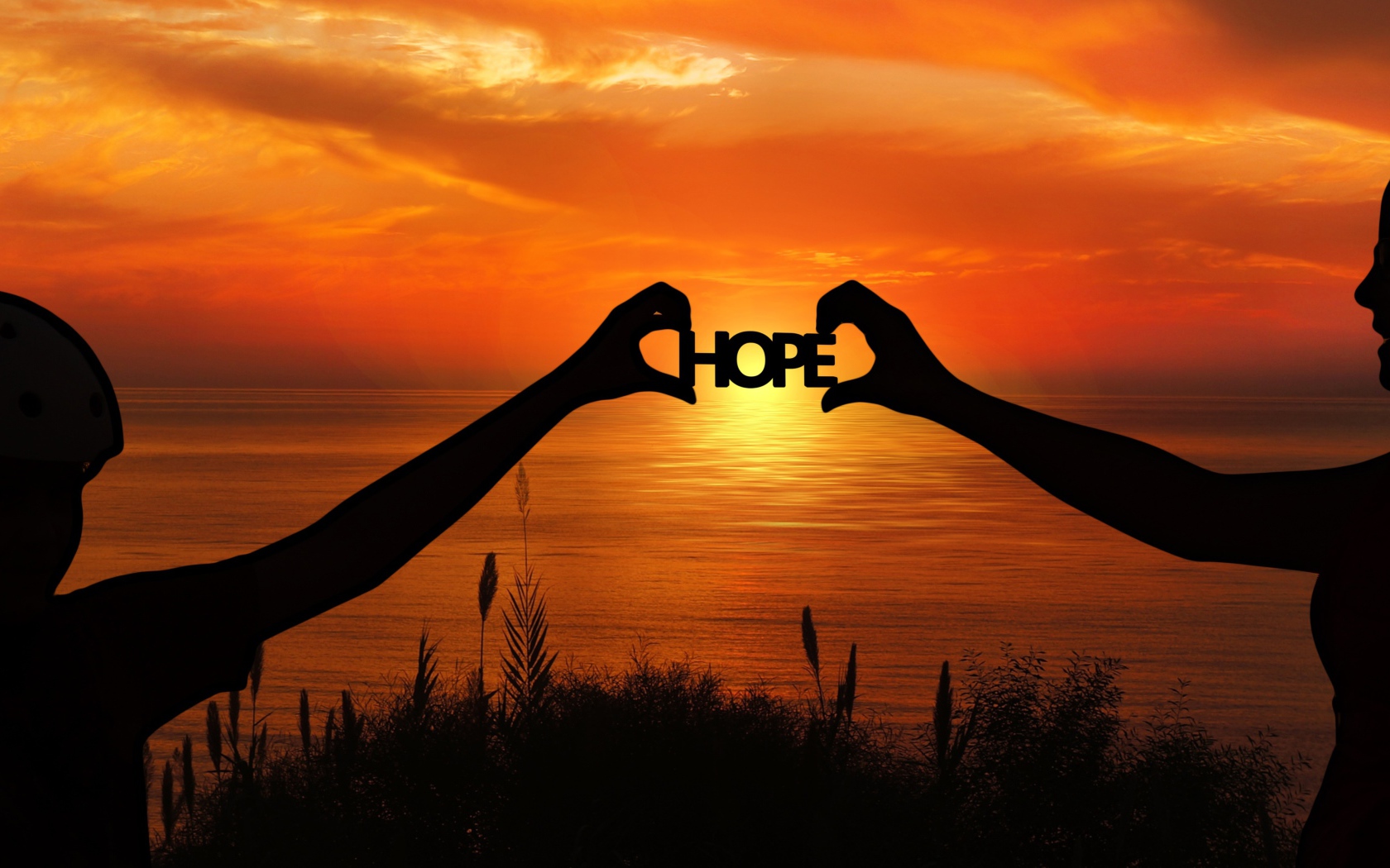 Силуэты пары держат в руках надпись HOPE на фоне заката