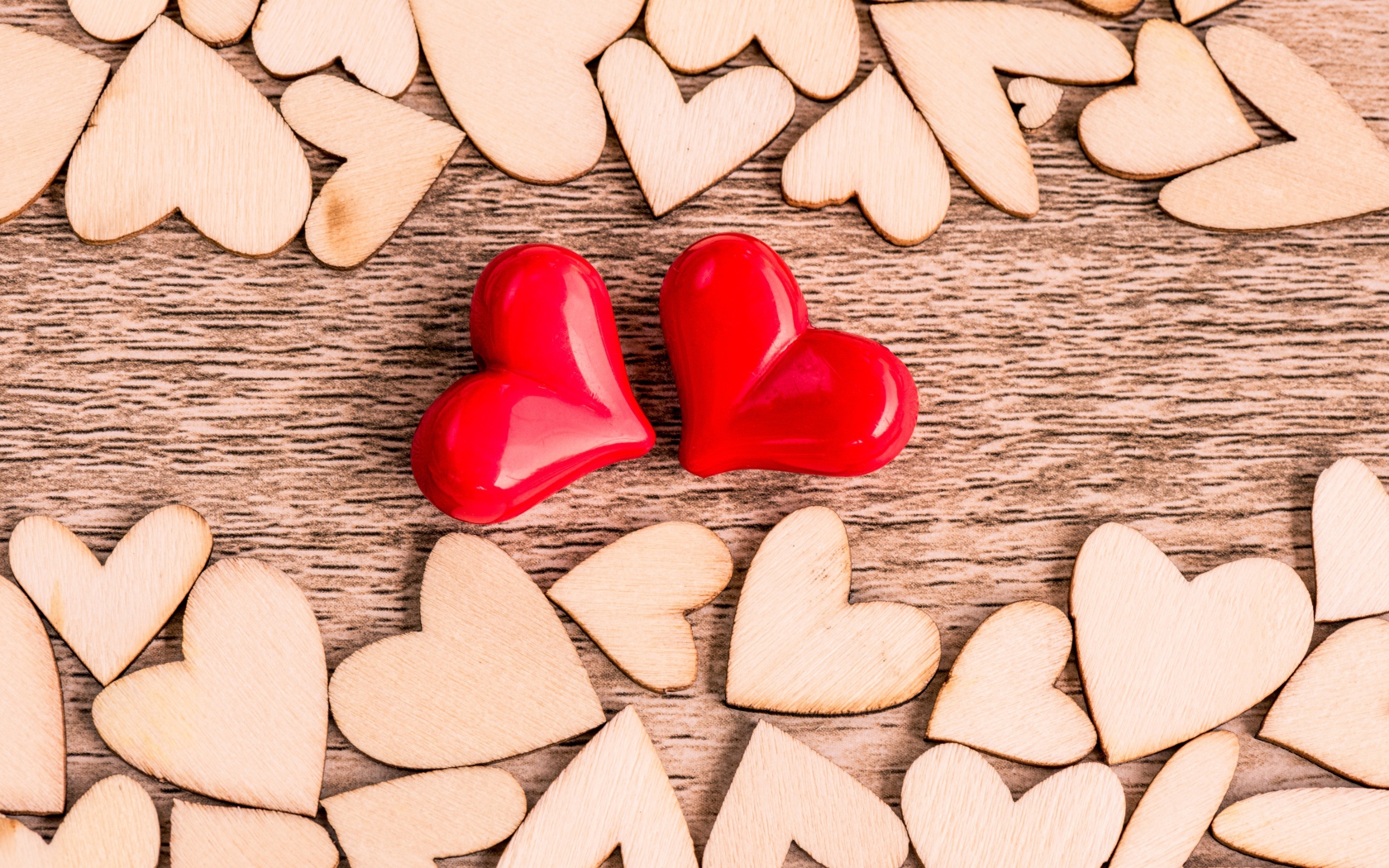 Two red hearts on a table with wooden hearts