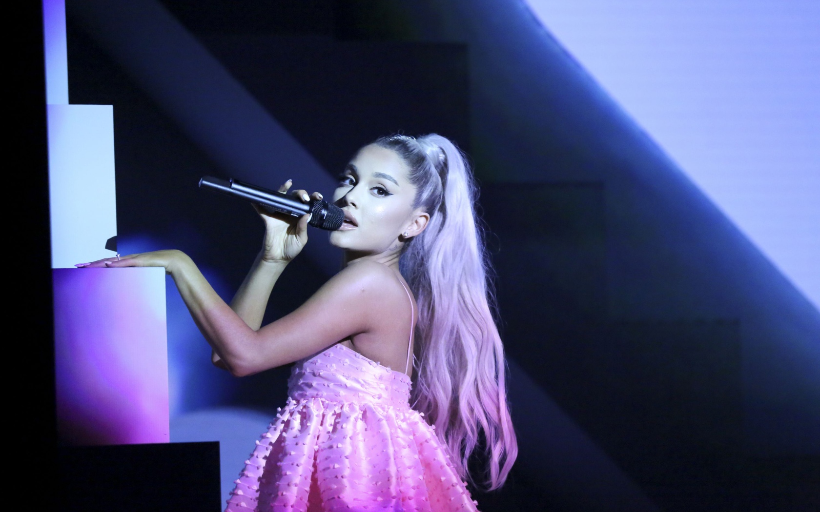Певица Ариана Гранде на сцене с микрофоном в розовом платье