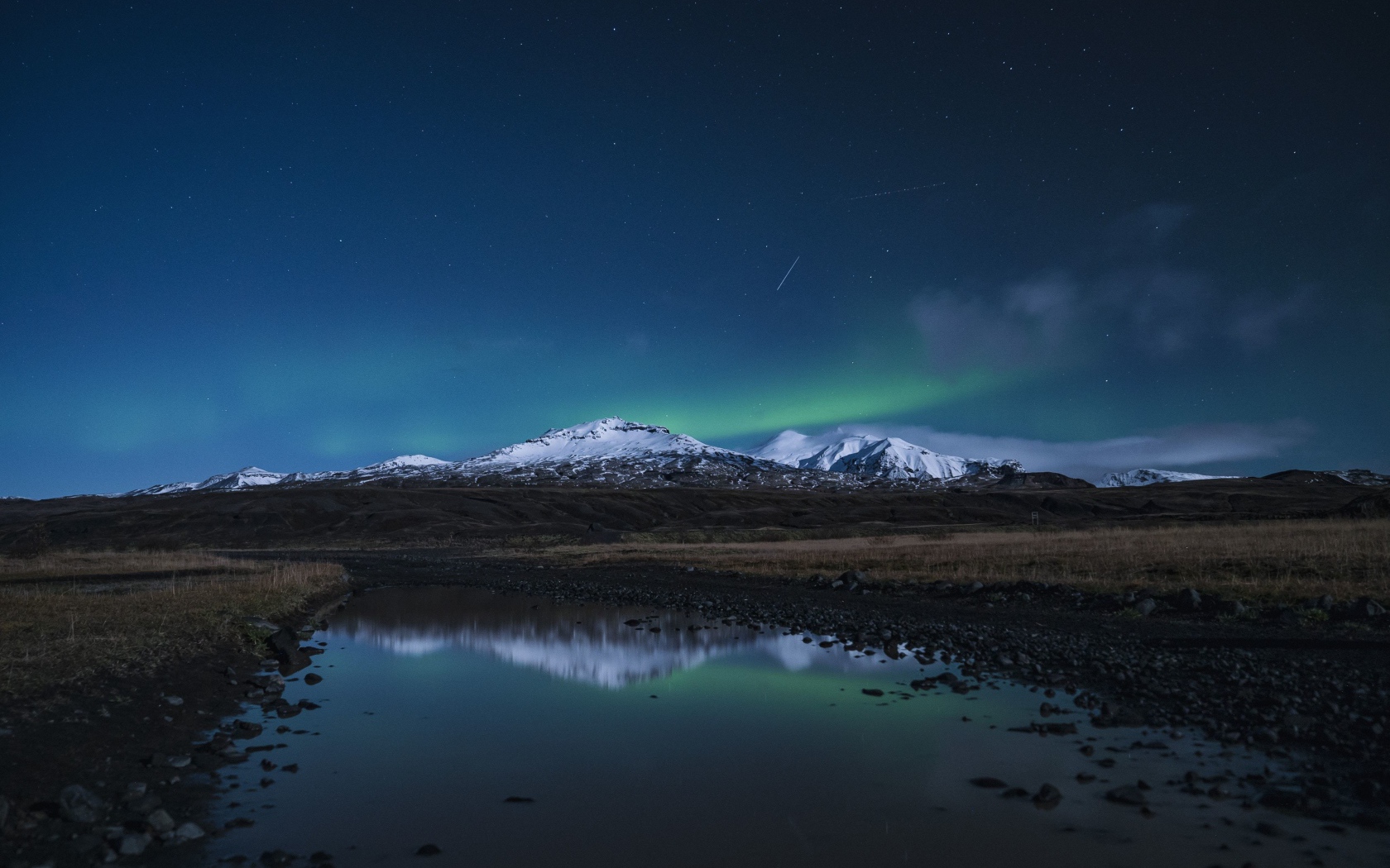 Горы и небо отражаются в луже на дороге ночью 