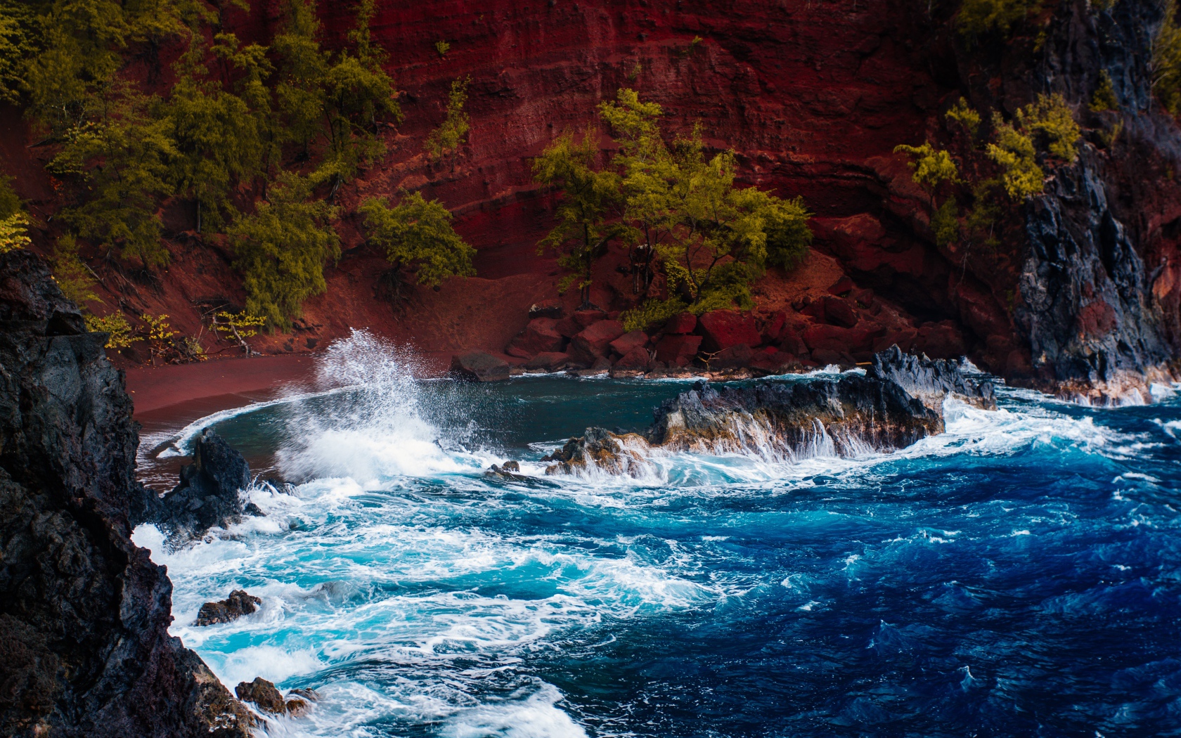 Грубое море брызгает камнями перед красным песчаным океанским заливом в Хане