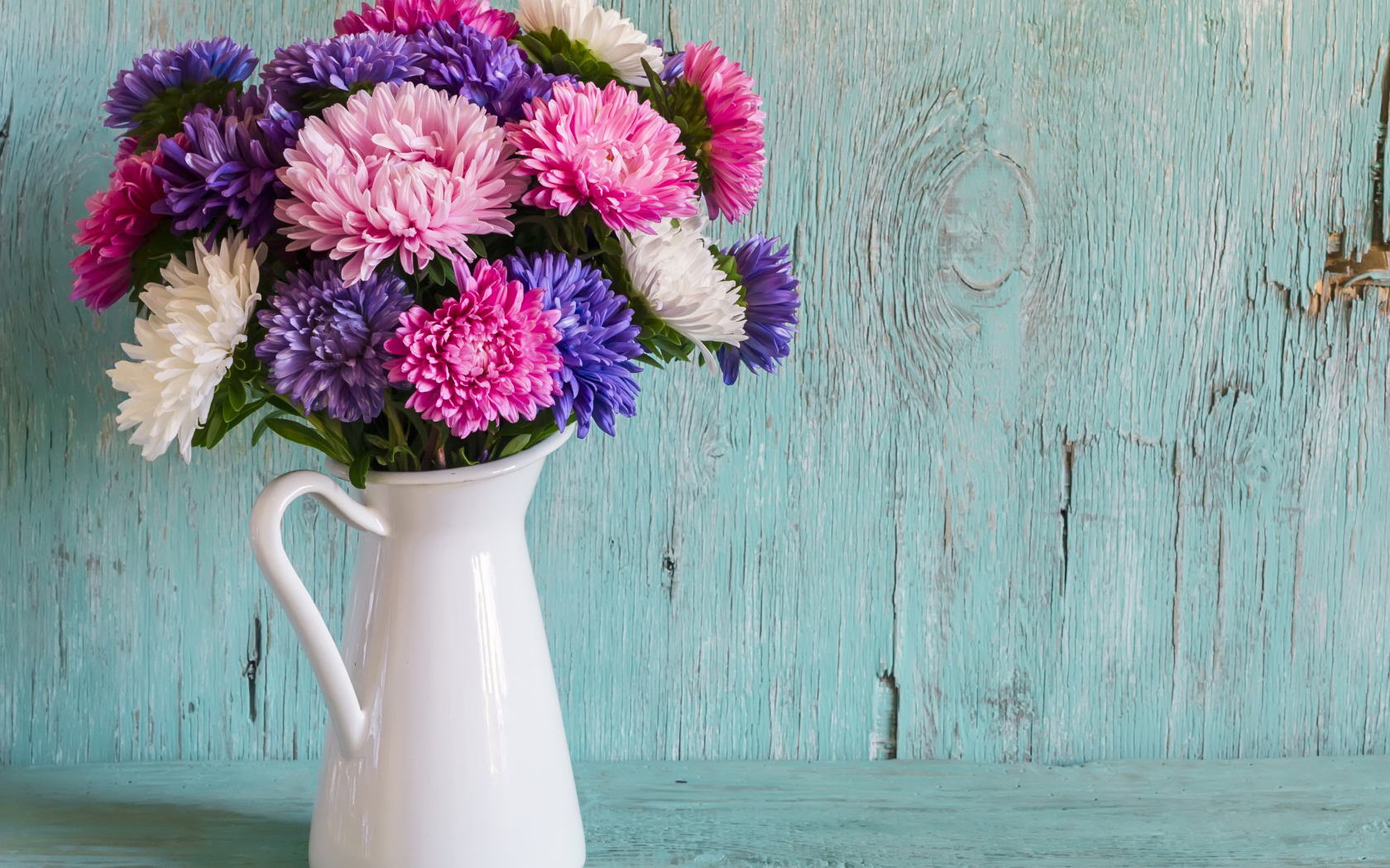 Разноцветные астры в вазе на деревянном фоне