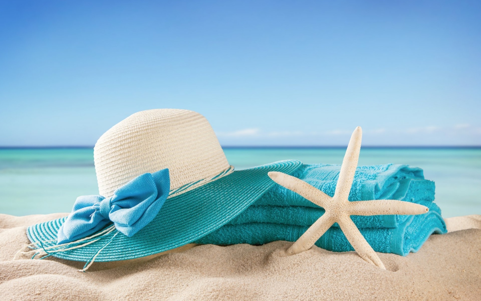 Большая шляпа, голубое полотенце и морская звезда на песке летом