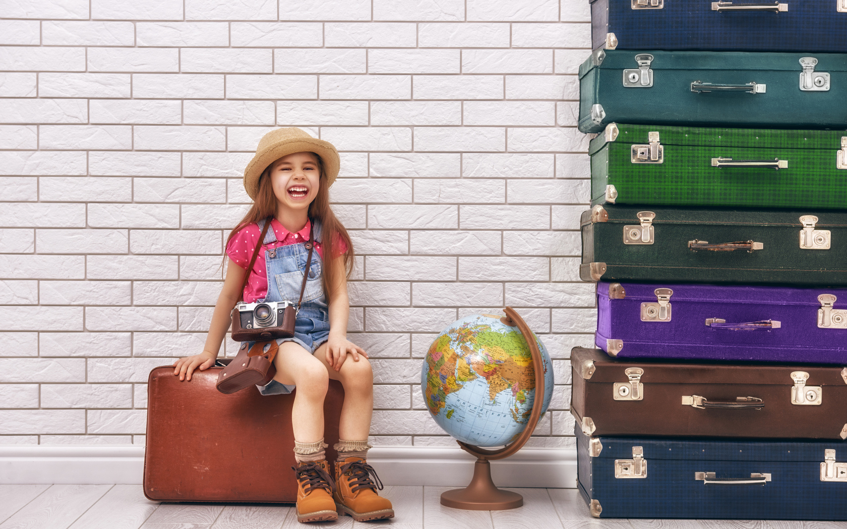 Маленькая девочка с фотоаппаратом сидит на чемодане