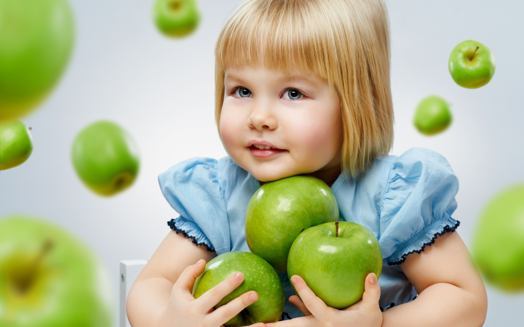 Маленькая девочка блондинка с зелеными яблоками