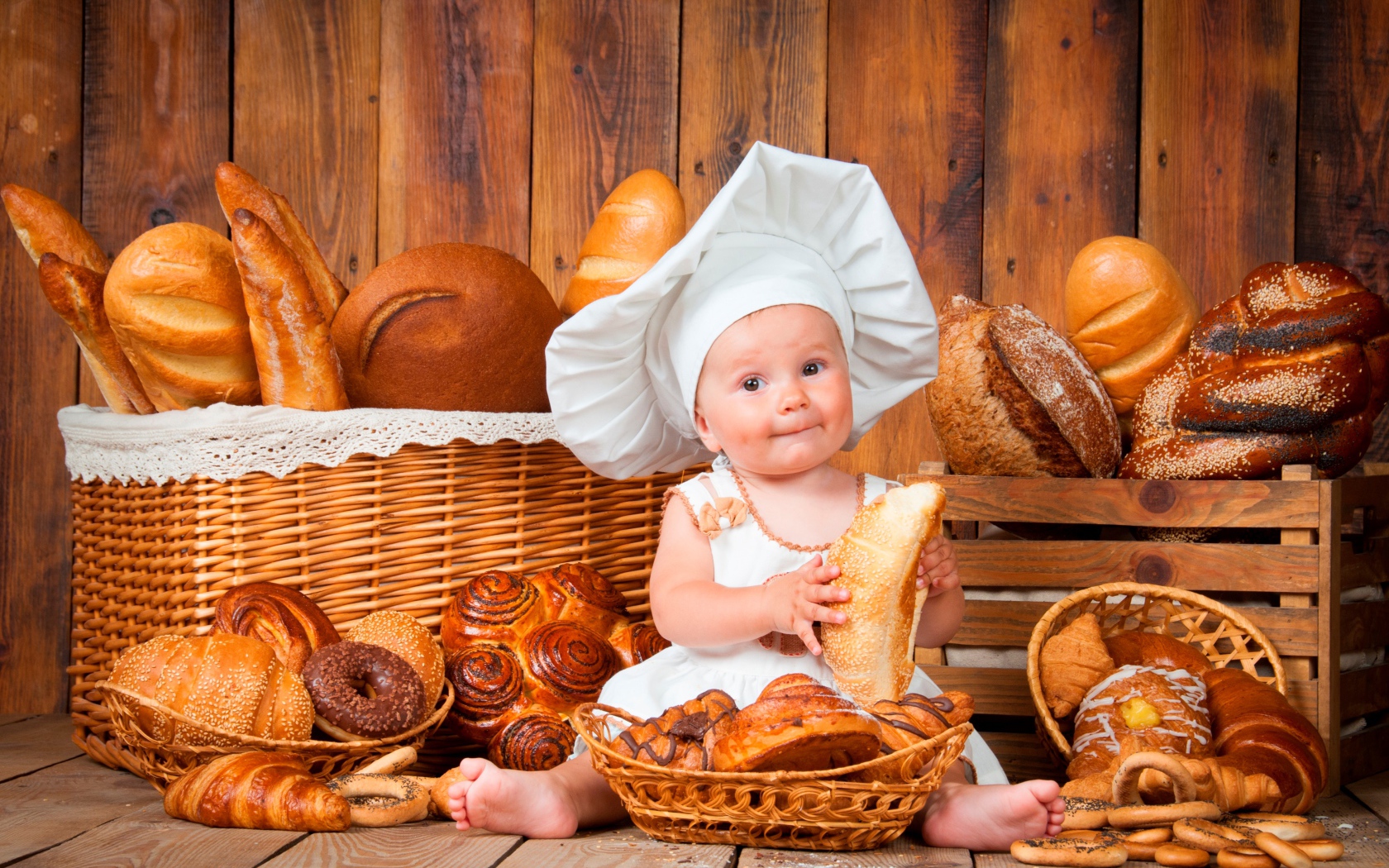 Маленький мальчик в костюме повара сидит на столе с выпечкой