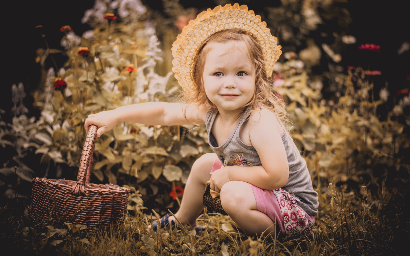 Маленькая девочка в шляпе сидит на траве с корзиной