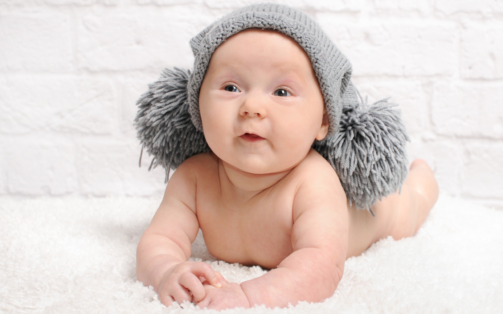 Улыбающийся грудной ребенок в серой шапке с бубонами