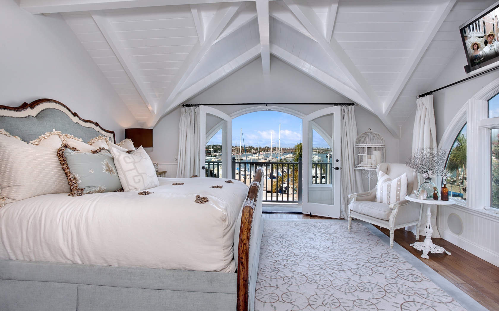 Белая спальня с большой высокой кроватью и балконом 