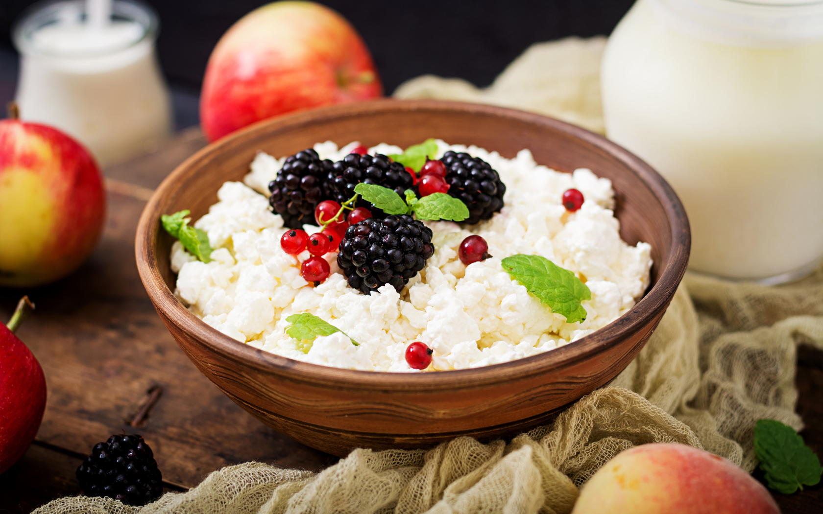 Творог с ягодами в деревянной миске на столе с яблоками
