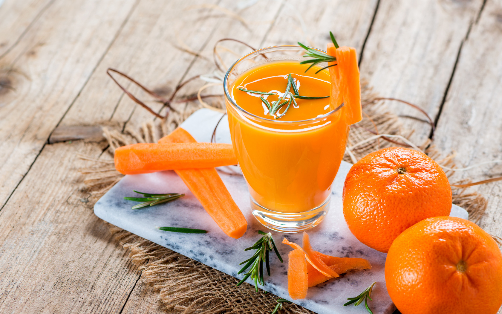 Два апельсина на столе со стаканом морковного сока