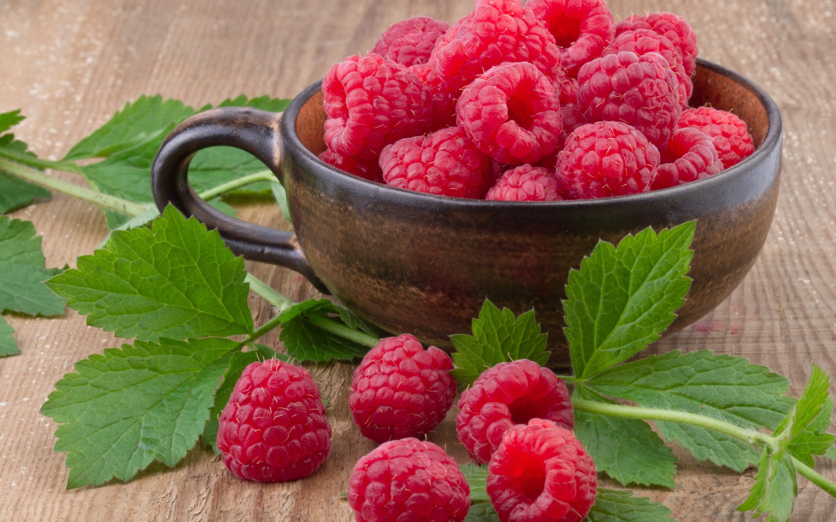 Чашка со свежей малиной на столе с зелеными листьями