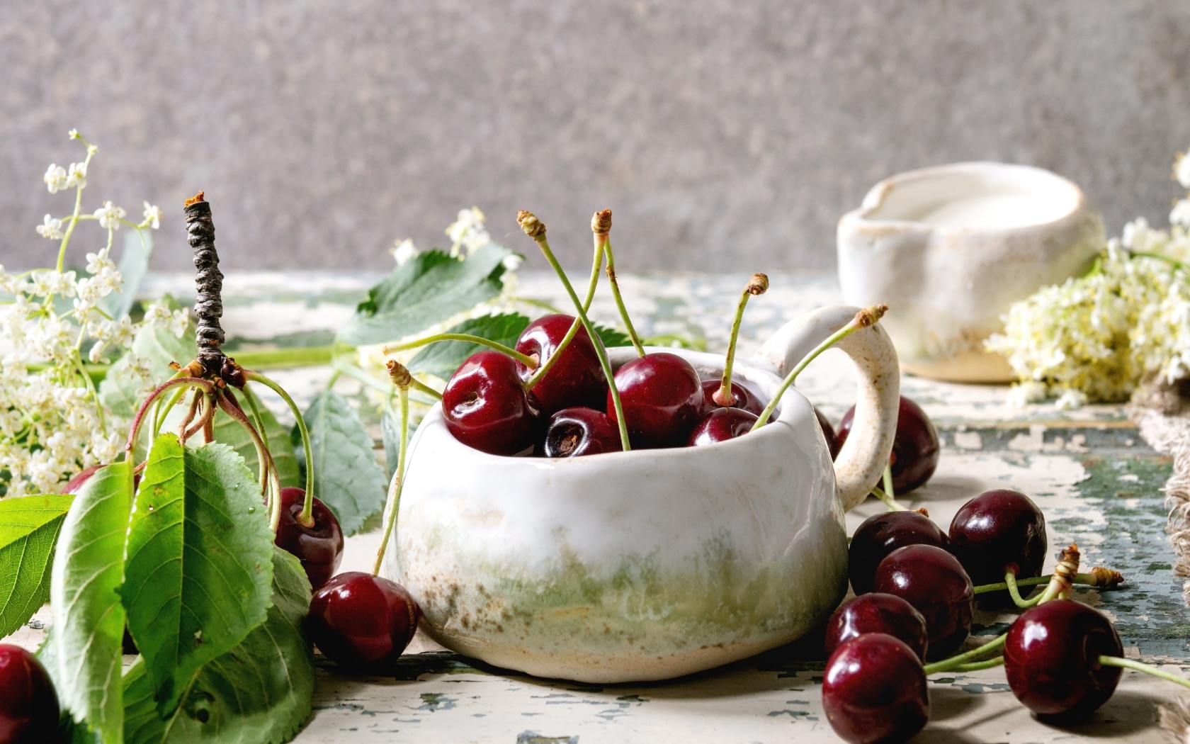 Спелые красные черешни на столе в белом чайнике