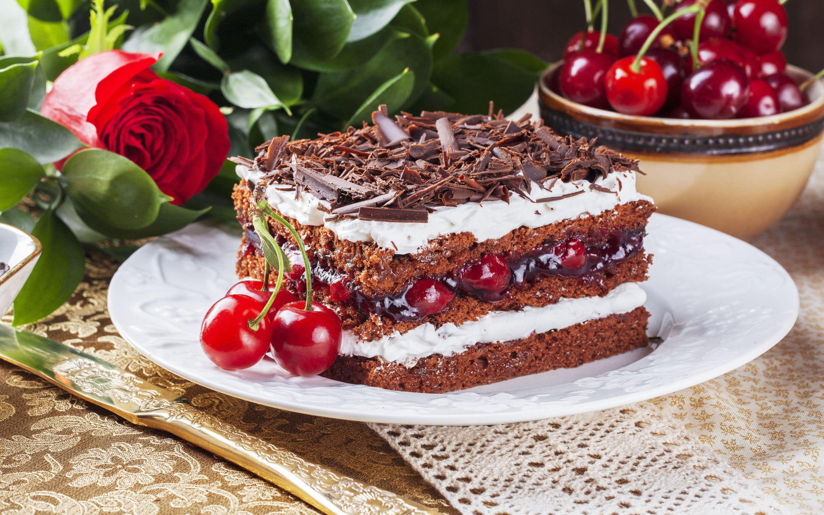 Кусок торта с вишней, шоколадной крошкой на столе с розой