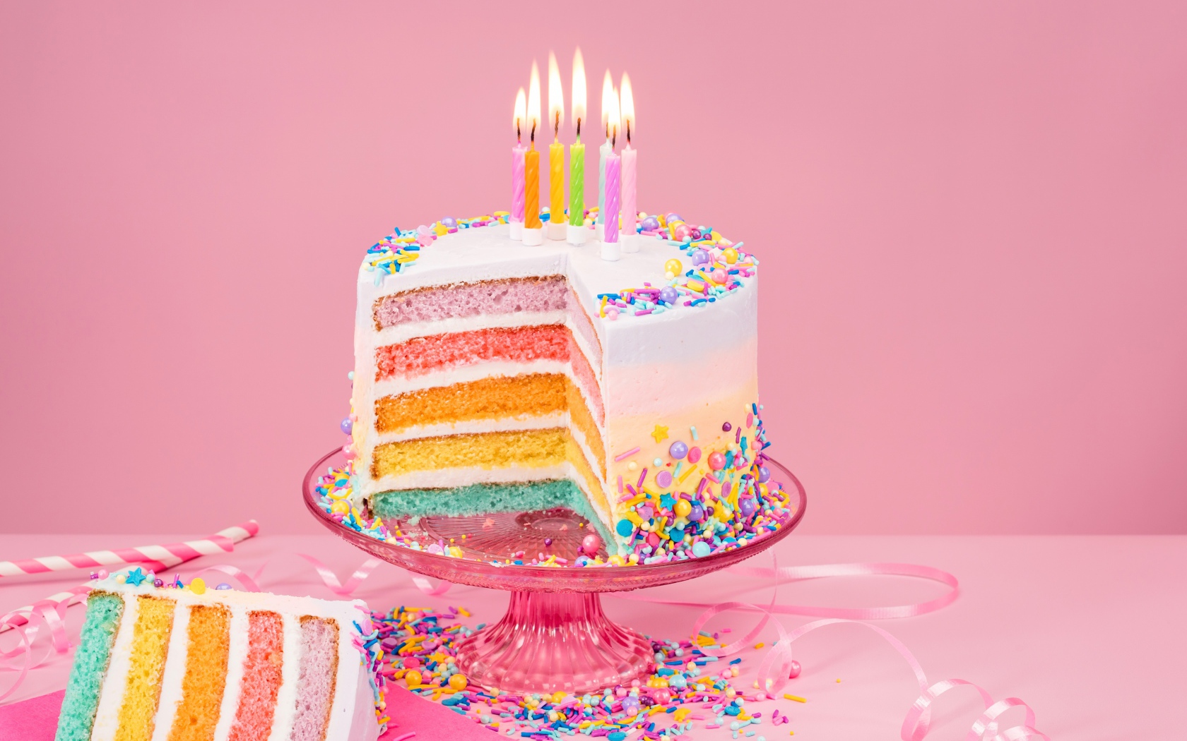 Разноцветный праздничный торт со свечами на розовом фоне
