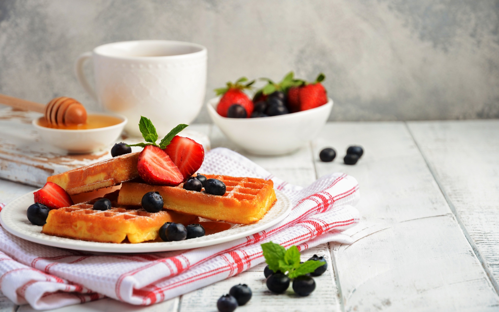 Сладкие вафли с ягодами черники и клубники на столе с медом и чаем