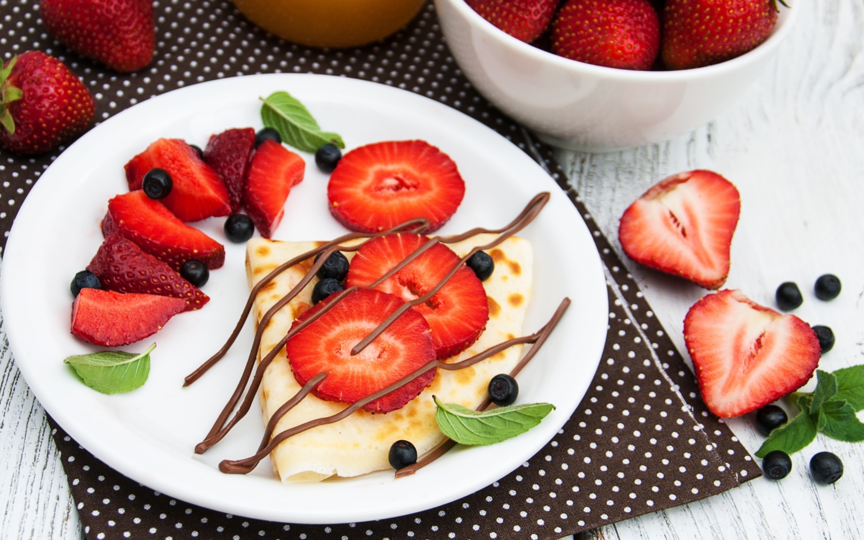 Тонкий блинчик на тарелке с шоколадом, ягодами клубники и черники