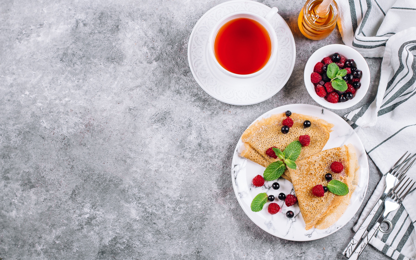 Тонкие блинчики на столе с ягодами, чаем и медом