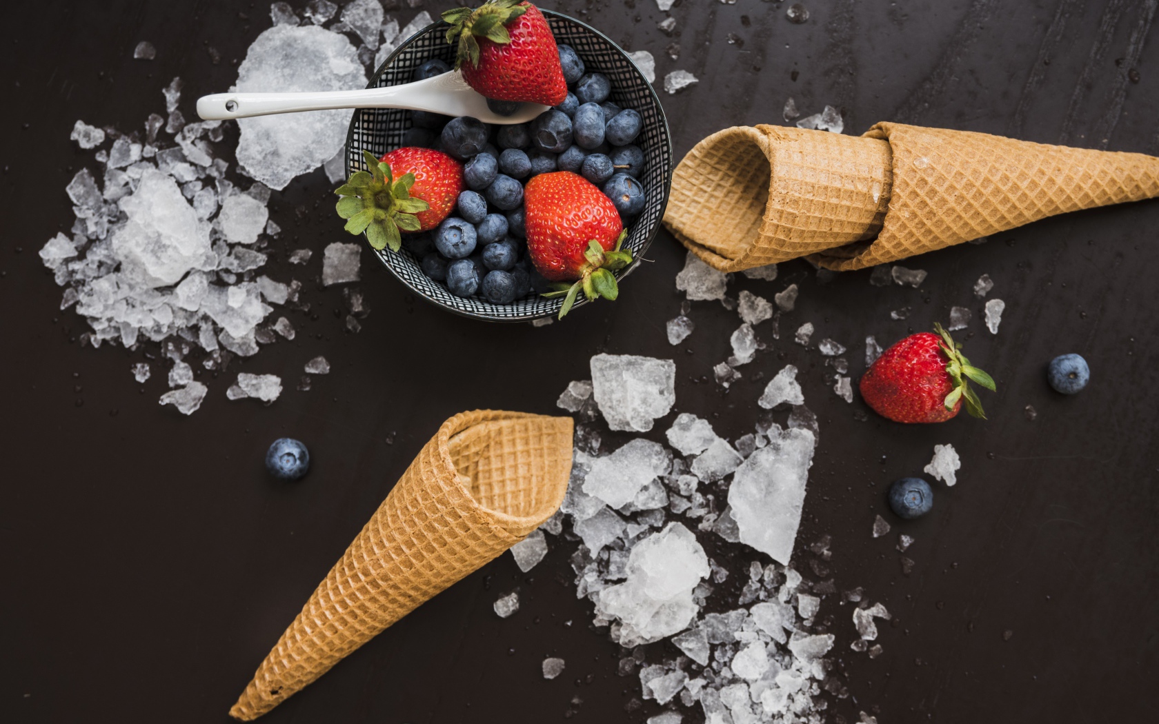 Вафельные рожки на столе со льдом и ягодами черники и клубники