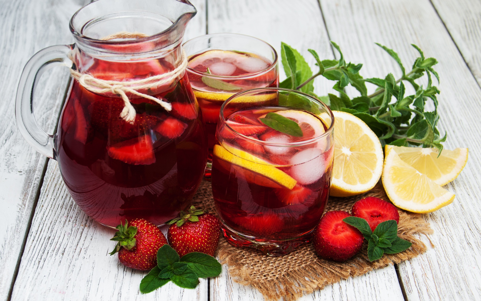 Два стакана мохито на столе с графином, лимоном, клубникой и мятой