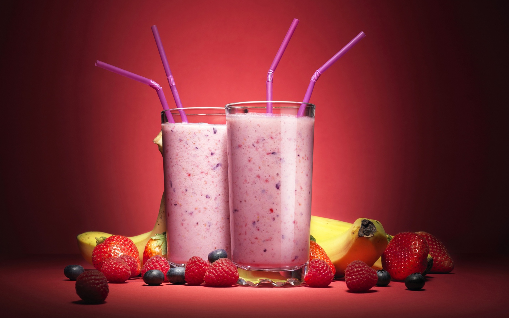Два стакана смузи на розовом фоне с ягодами и бананами 