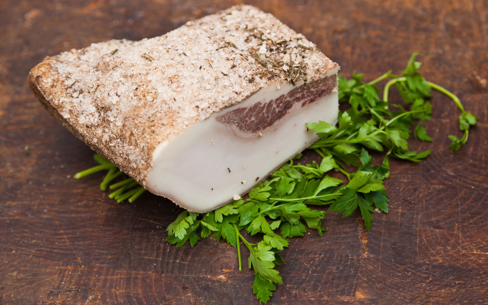 Кусок сала со специями на столе с зеленью петрушки