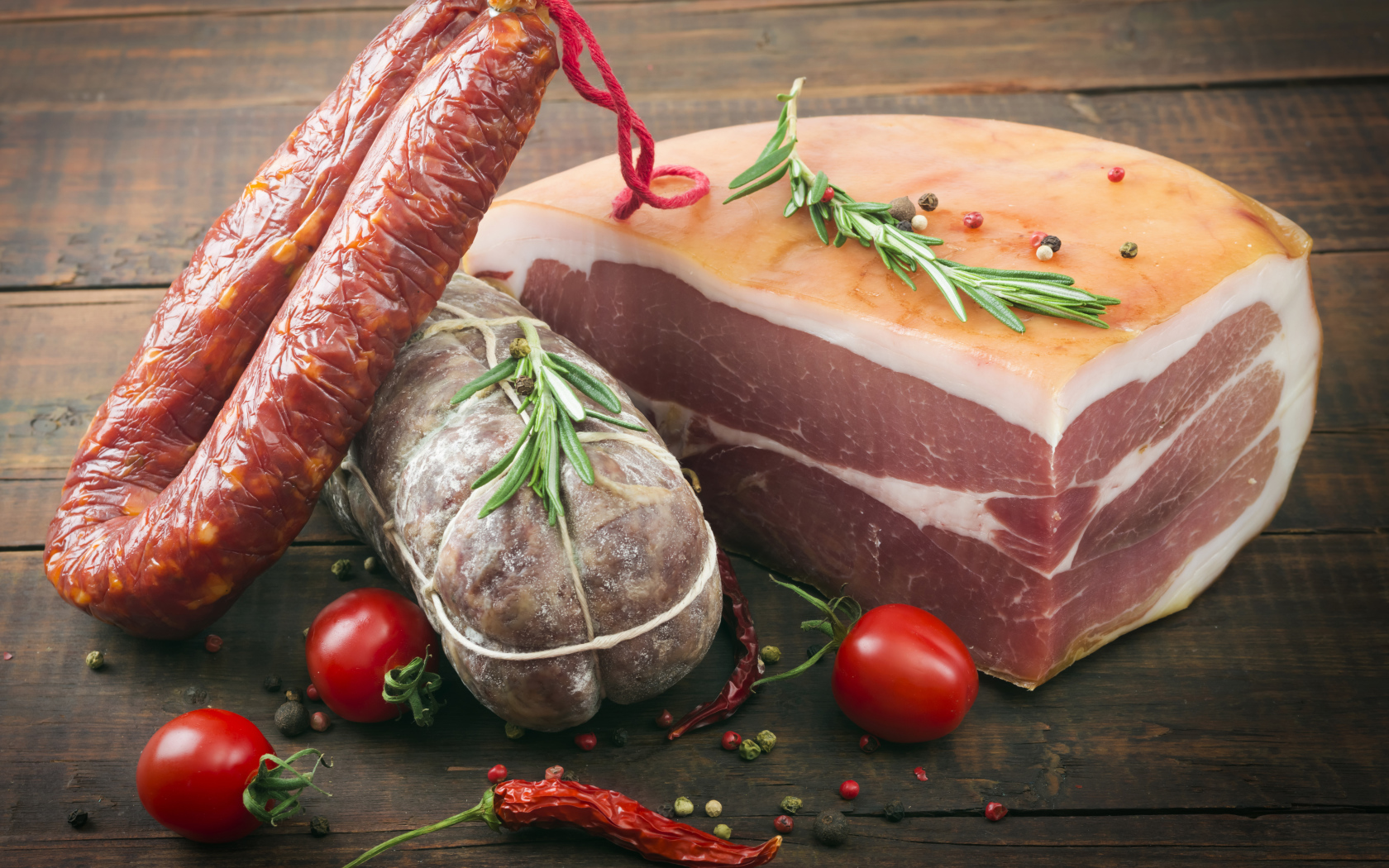 Кусок мяса и колбаса на деревянном столе с помидорами и специями