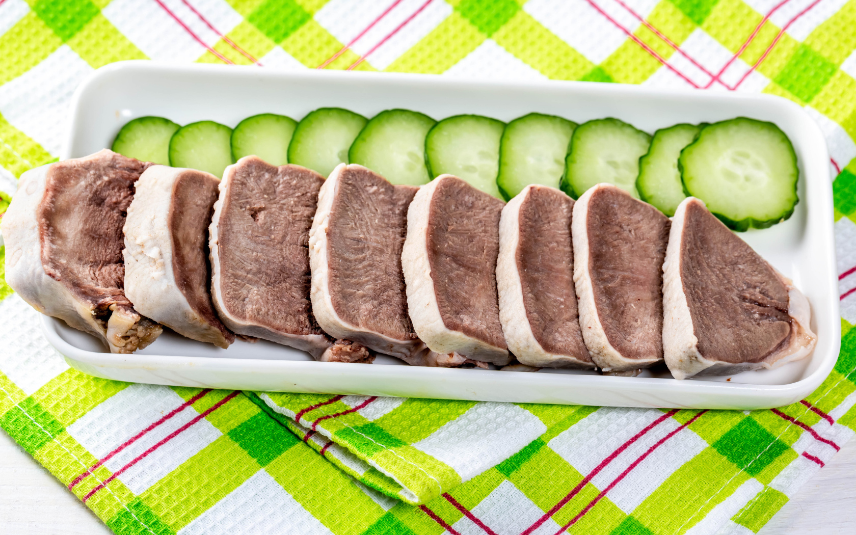 Вареный язык на тарелке со свежими огурцами