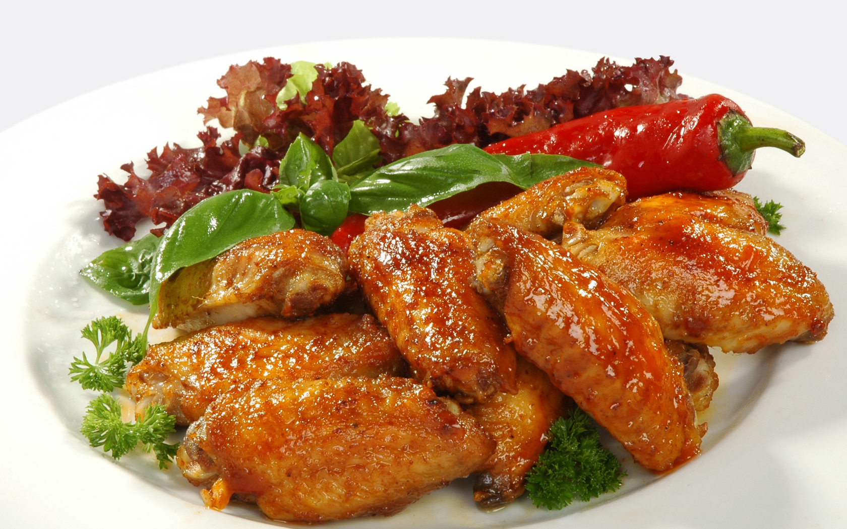 Жареные куриные крылышки на тарелке с острым перцем и зеленью 