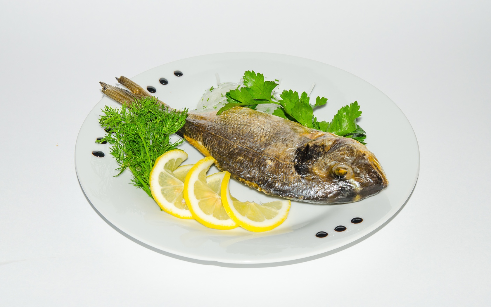 Запеченная рыба на тарелке с лимоном и зеленью 