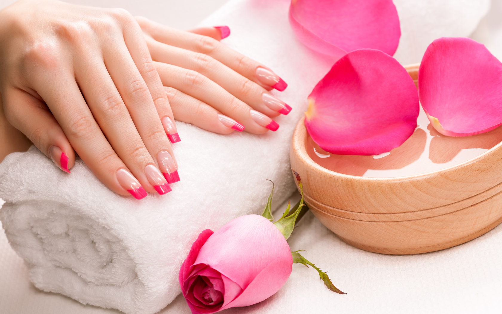 Женские руки с красивым маникюром лежат на белом полотенце на столе с розой