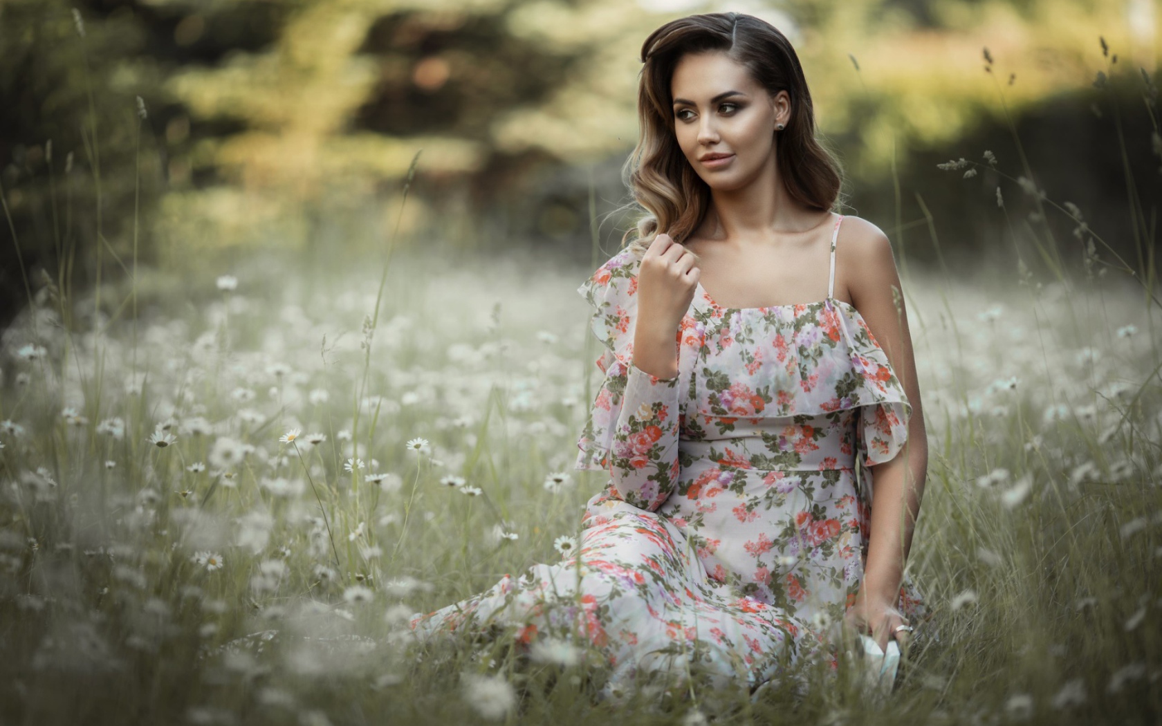 Красивая девушка в сарафане сидит на поляне с ромашками 